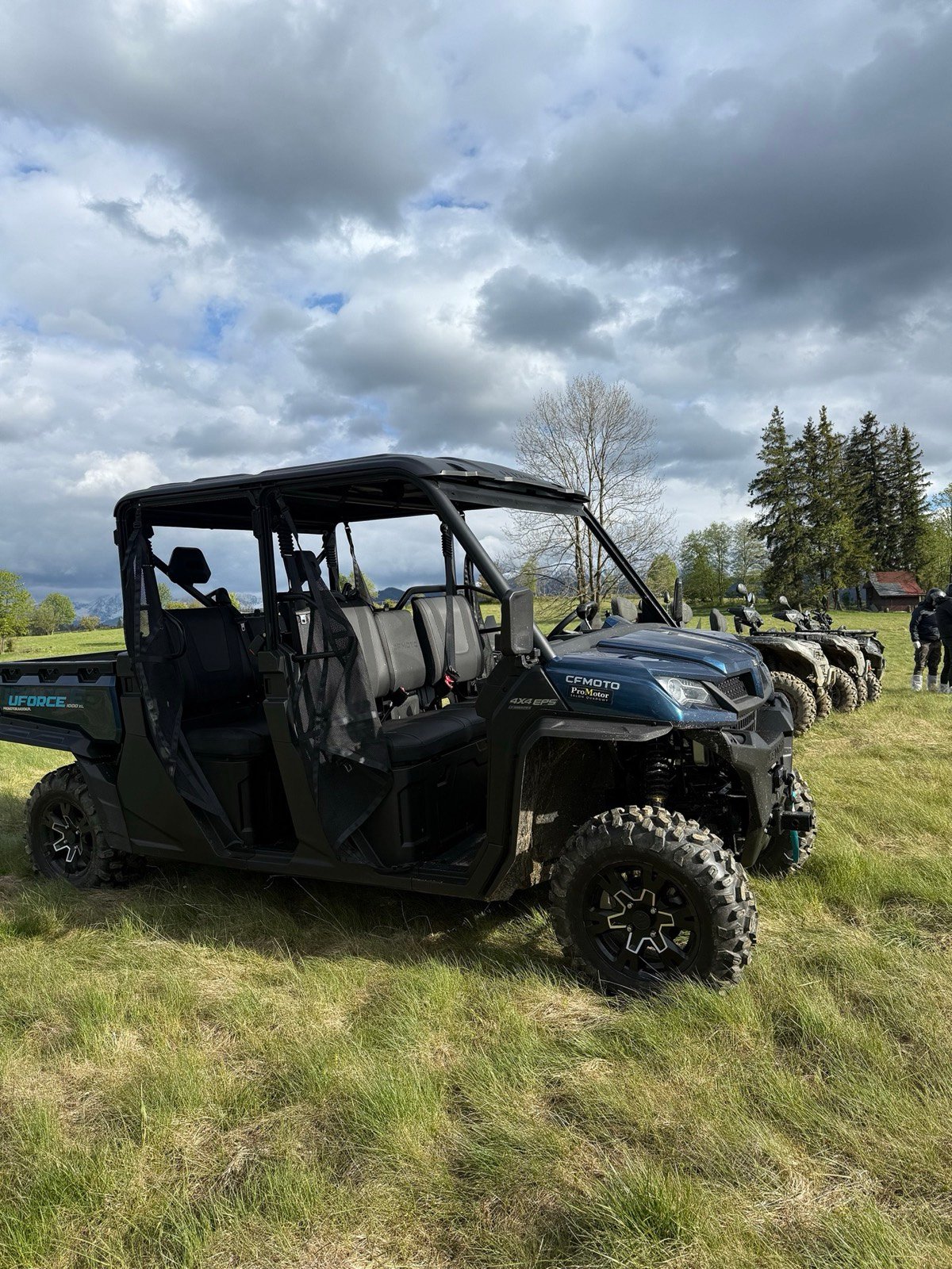 A six-seat CFMoto buggy with two rows of seats on a meadow, quads parked beside it