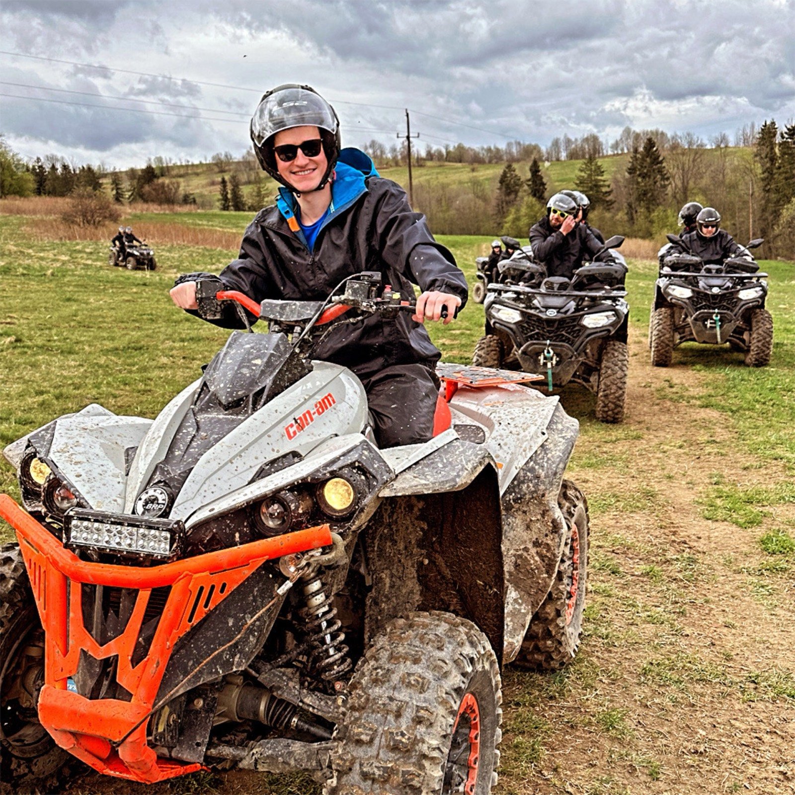 A smiling rider in a helmet on a Can-Am quad on a dirt track, more quads behind