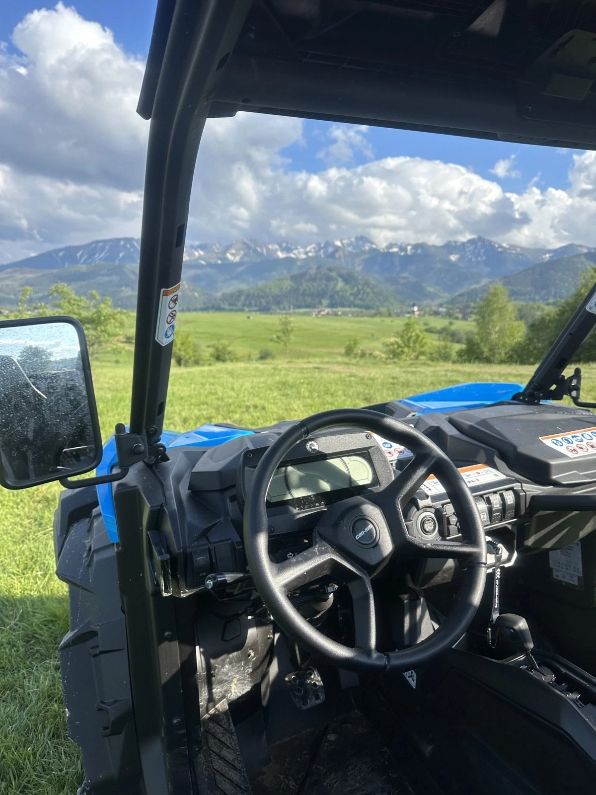 View from behind the wheel of a blue buggy over a meadow to the snow-capped Tatra peaks