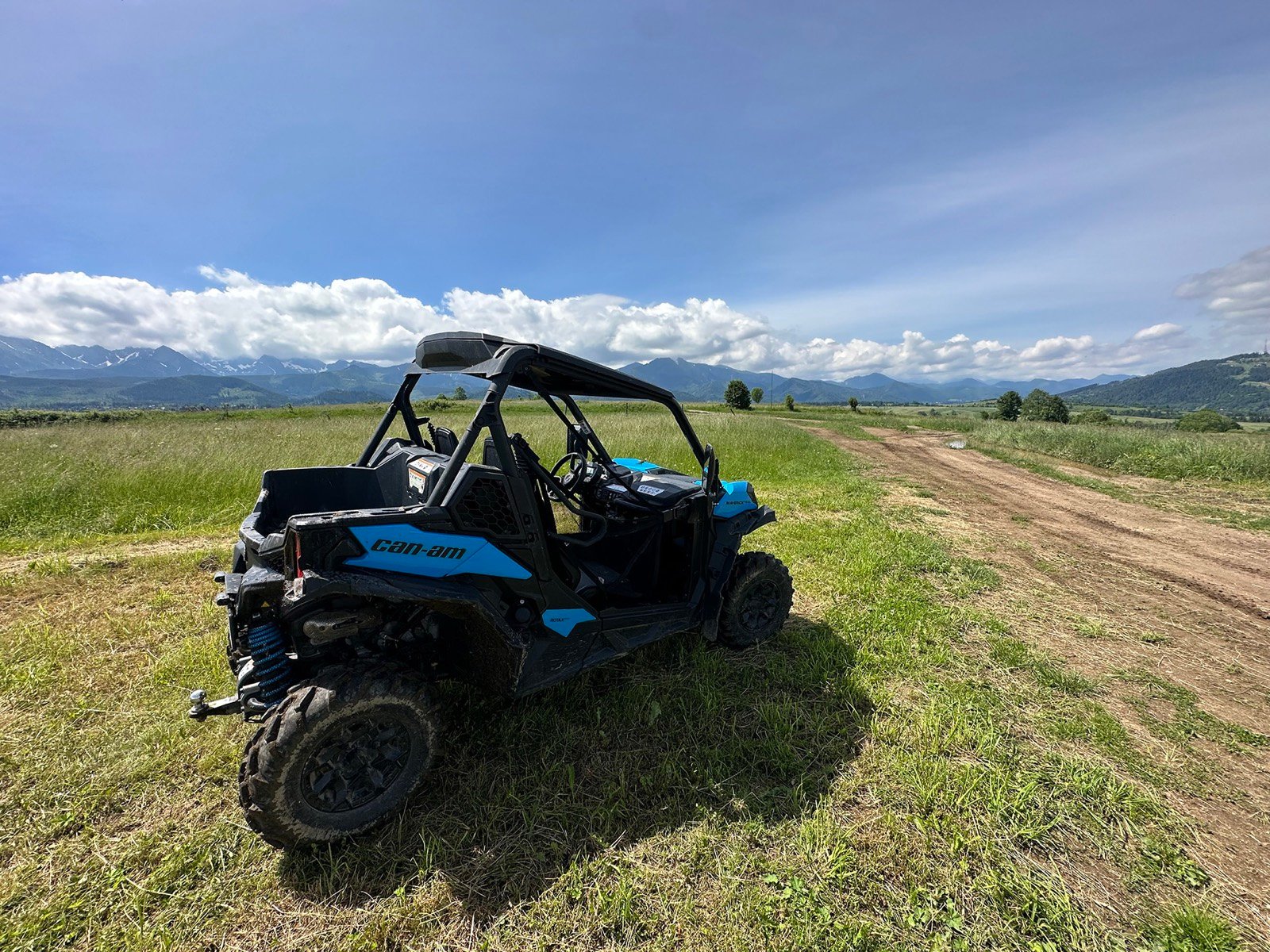 A blue buggy on a field track with meadows and the Tatra range behind