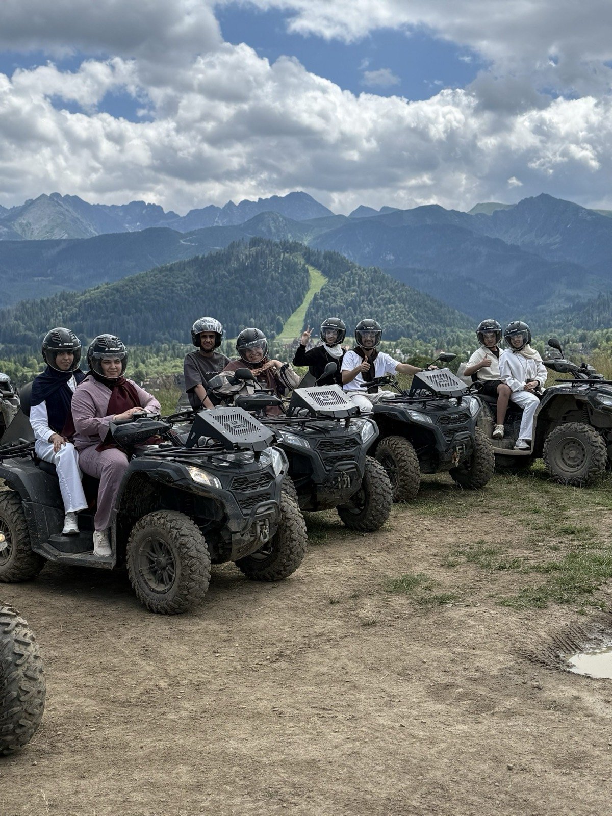 A group in helmets on quads lined up on a ridge with the Tatra panorama behind