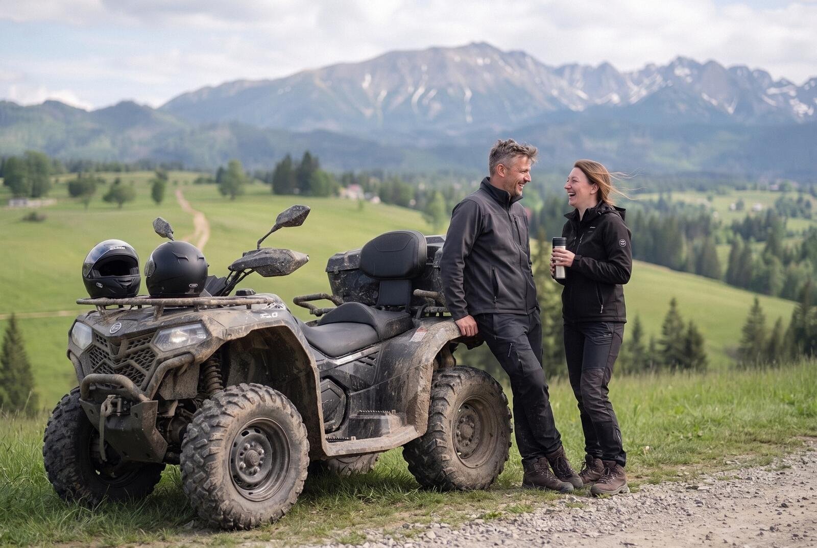 A couple chatting, leaning on a muddy quad at a stop by a gravel track, helmets on the handlebars, the Tatras behind