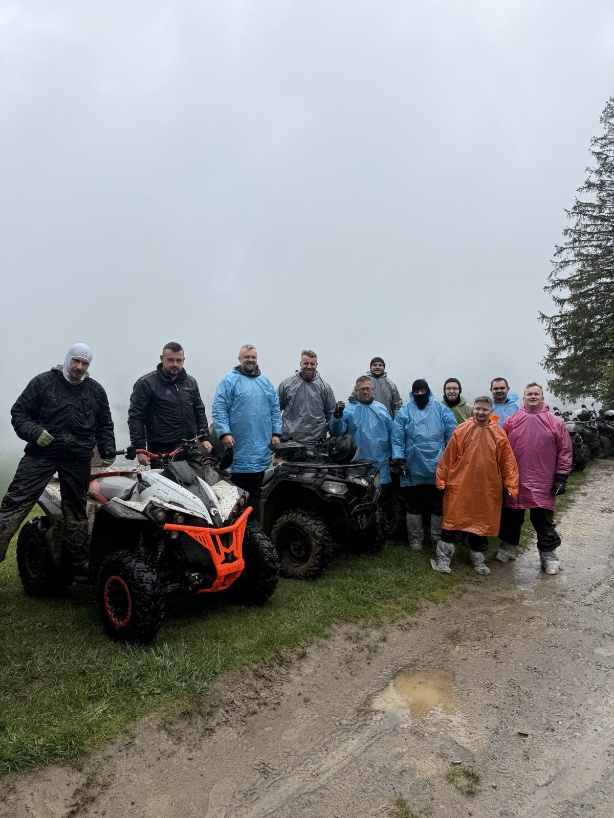 A group in rain jackets around a quad on a forest track on a rainy day