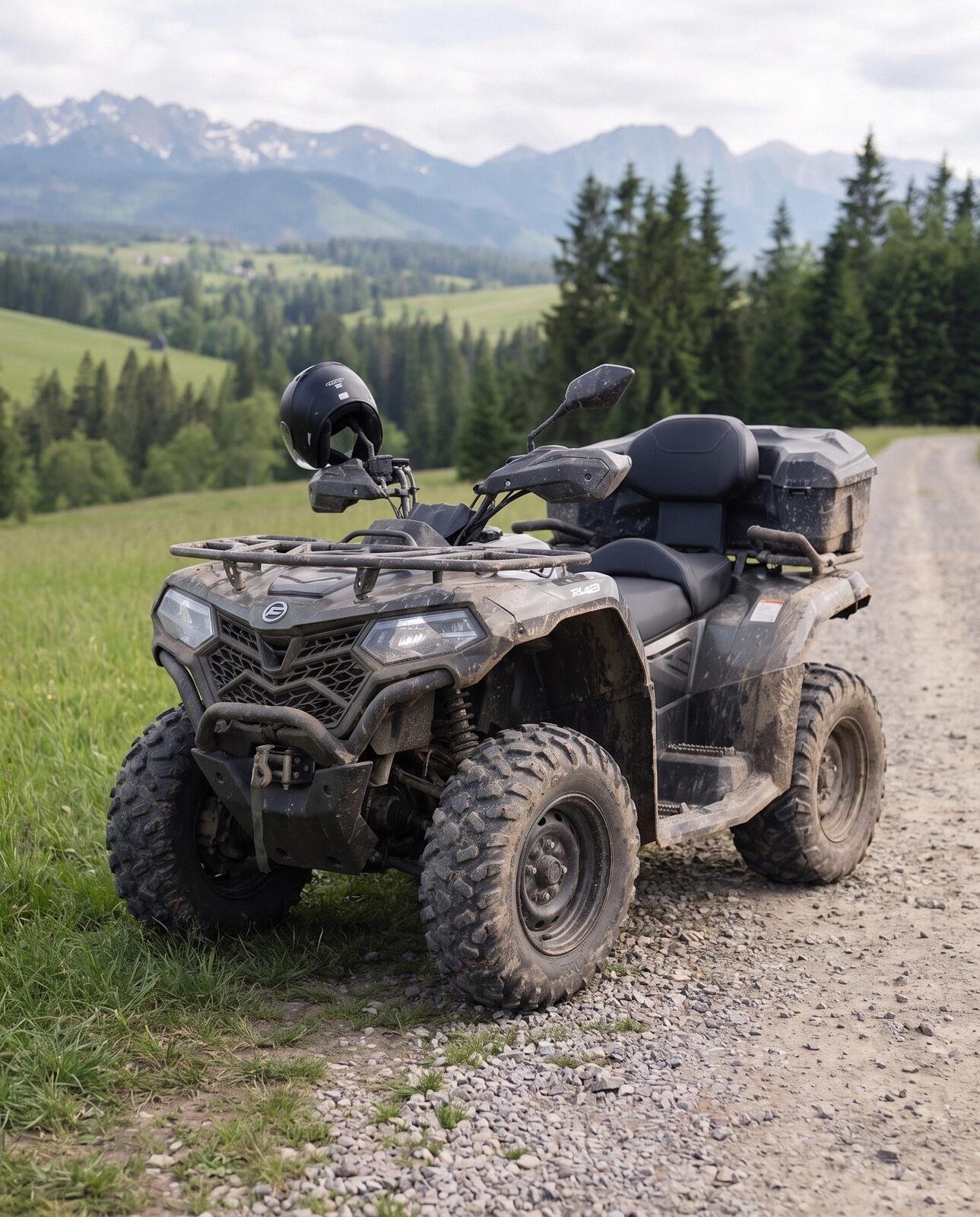 A muddy two-seater quad with a helmet on its mirror parked on a gravel track among spruces, the Tatras behind