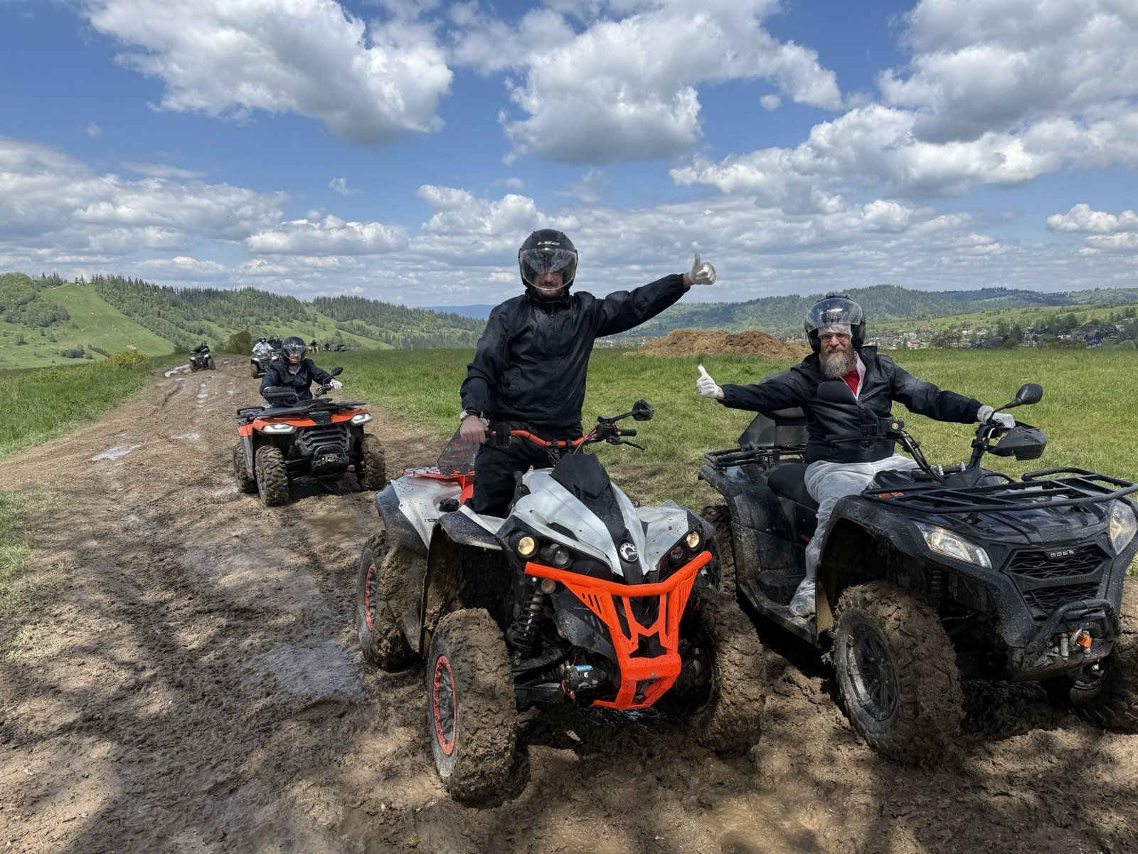 A rider in a helmet on a quad giving a thumbs up, another quad beside, green meadows and clouds over the Tatras behind