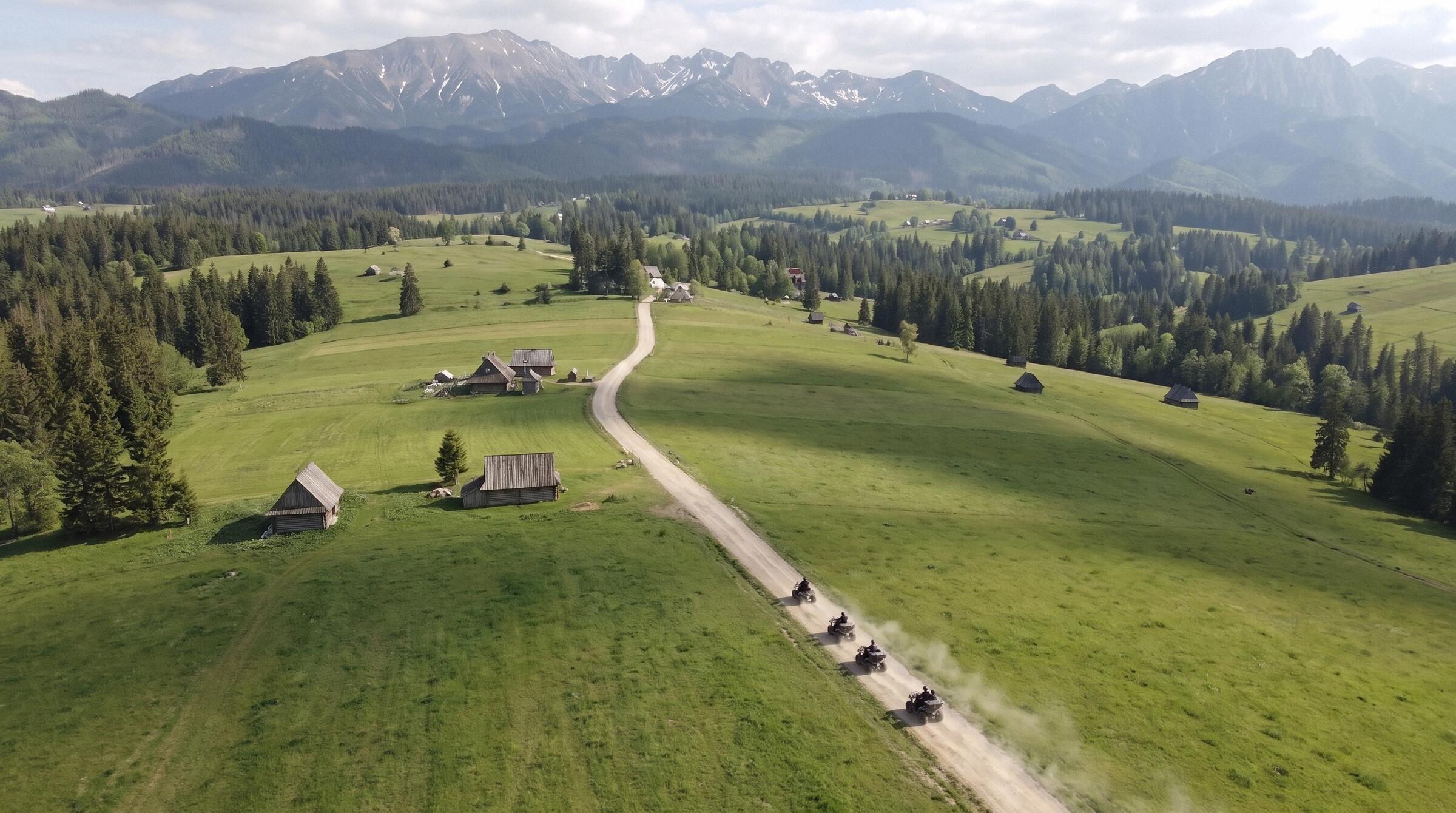Widok z drona: kolumna quadów jedzie szutrową drogą przez hale z drewnianymi szałasami, na horyzoncie Tatry