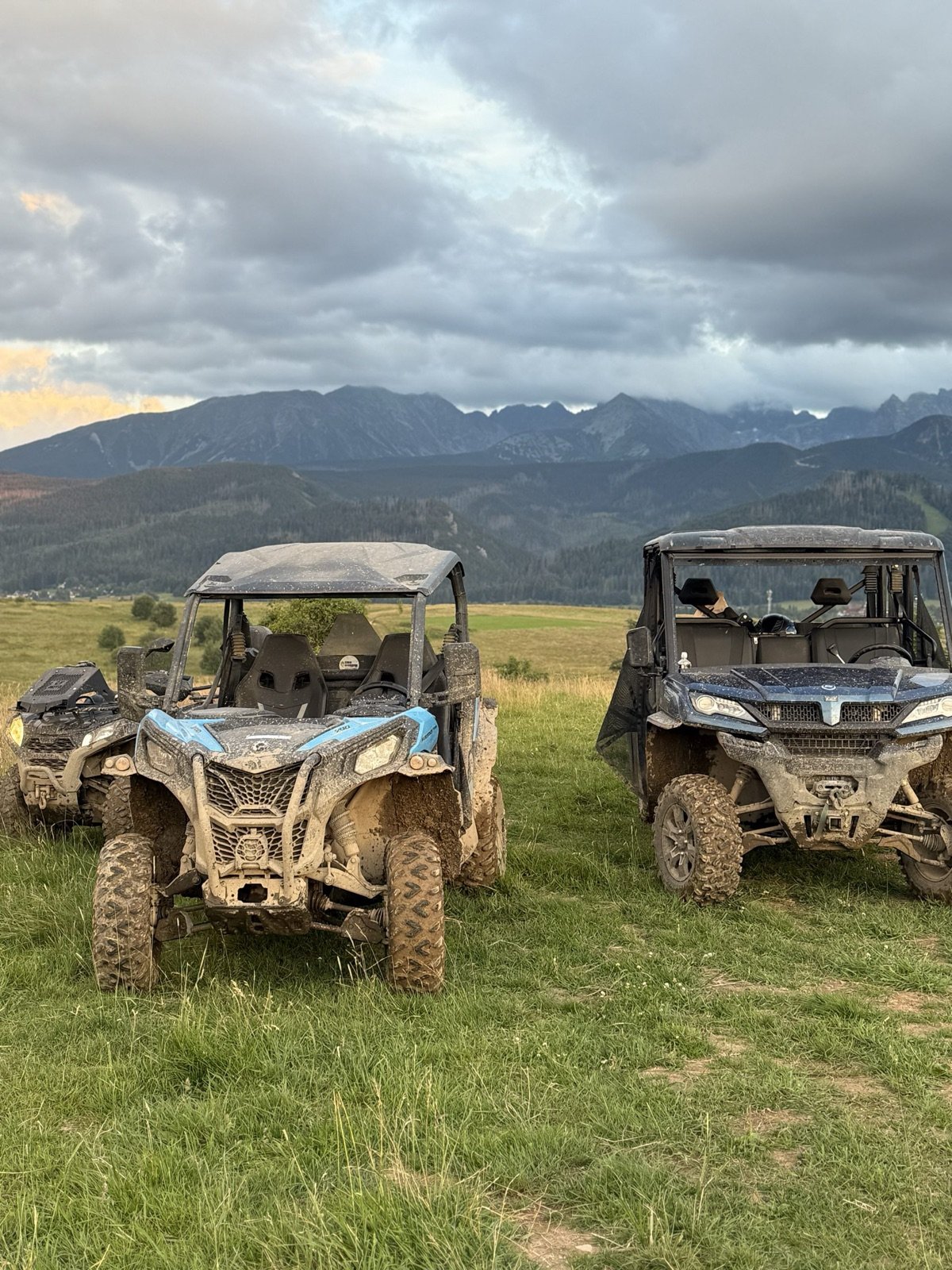 Two mud-covered buggies on a meadow at dusk with the Tatras on the horizon