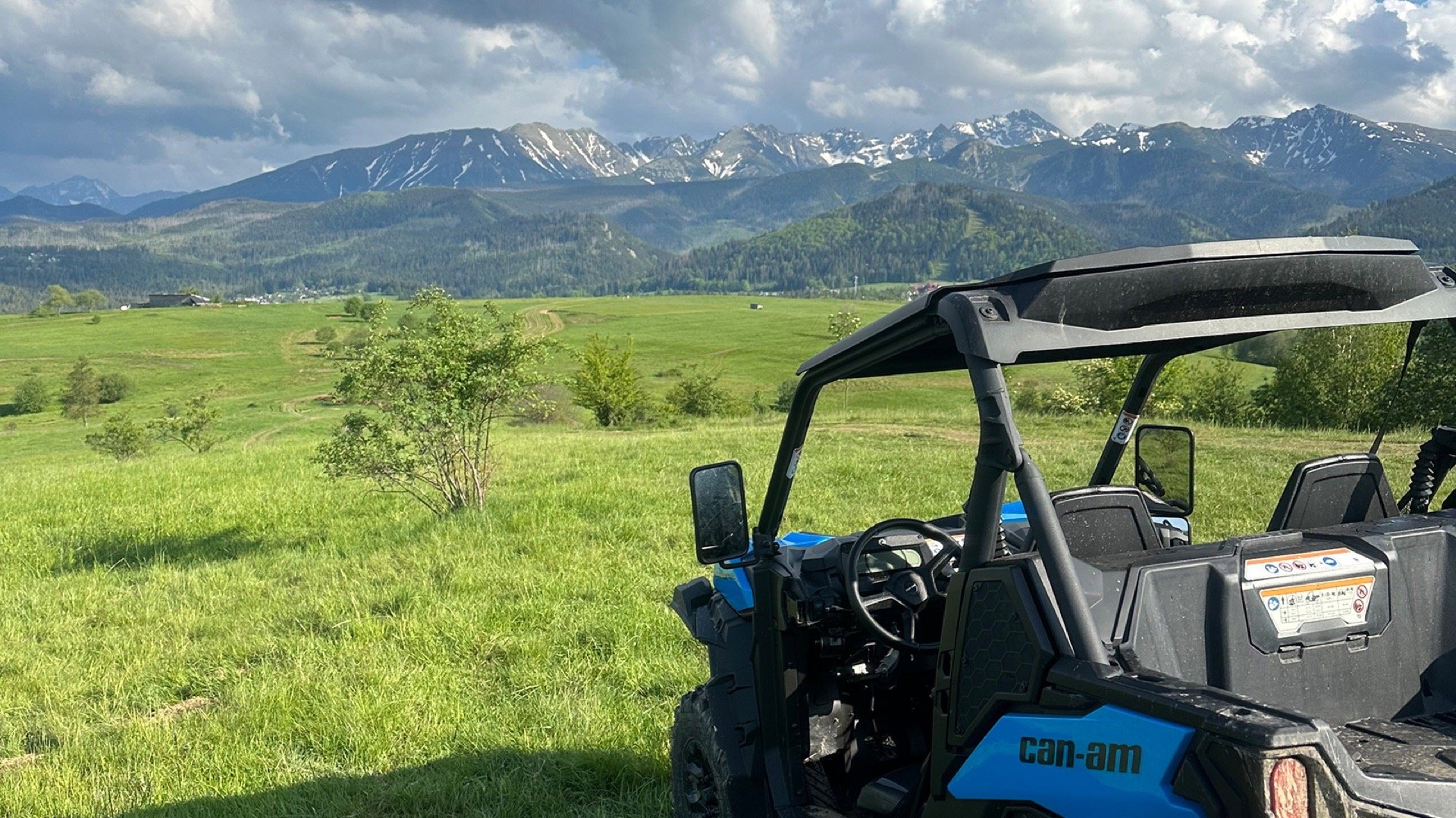 A blue Can-Am buggy on a meadow facing the Tatra peaks