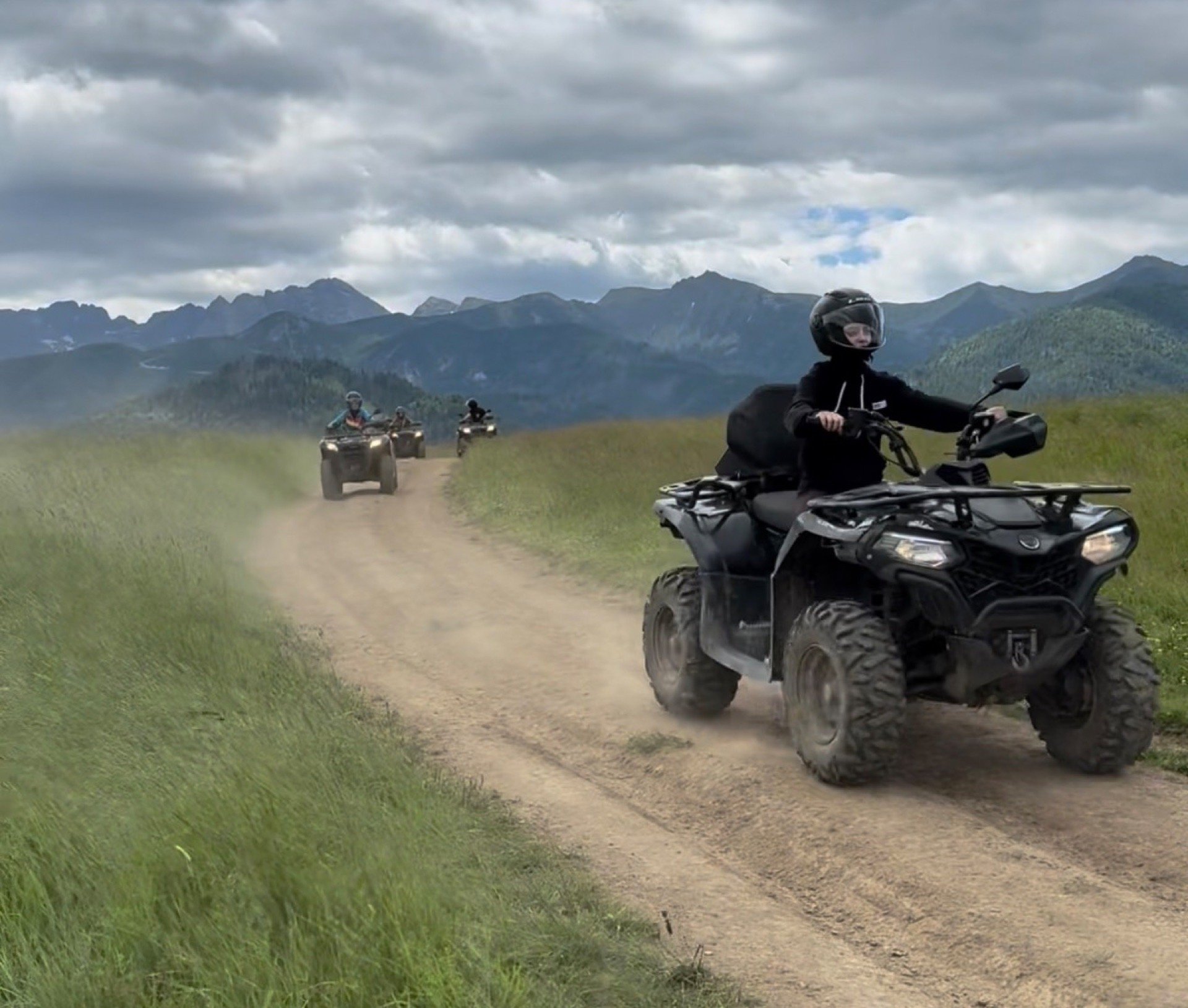 A quad in a cloud of dust on a dirt track, more quads behind, the Tatra range on the horizon