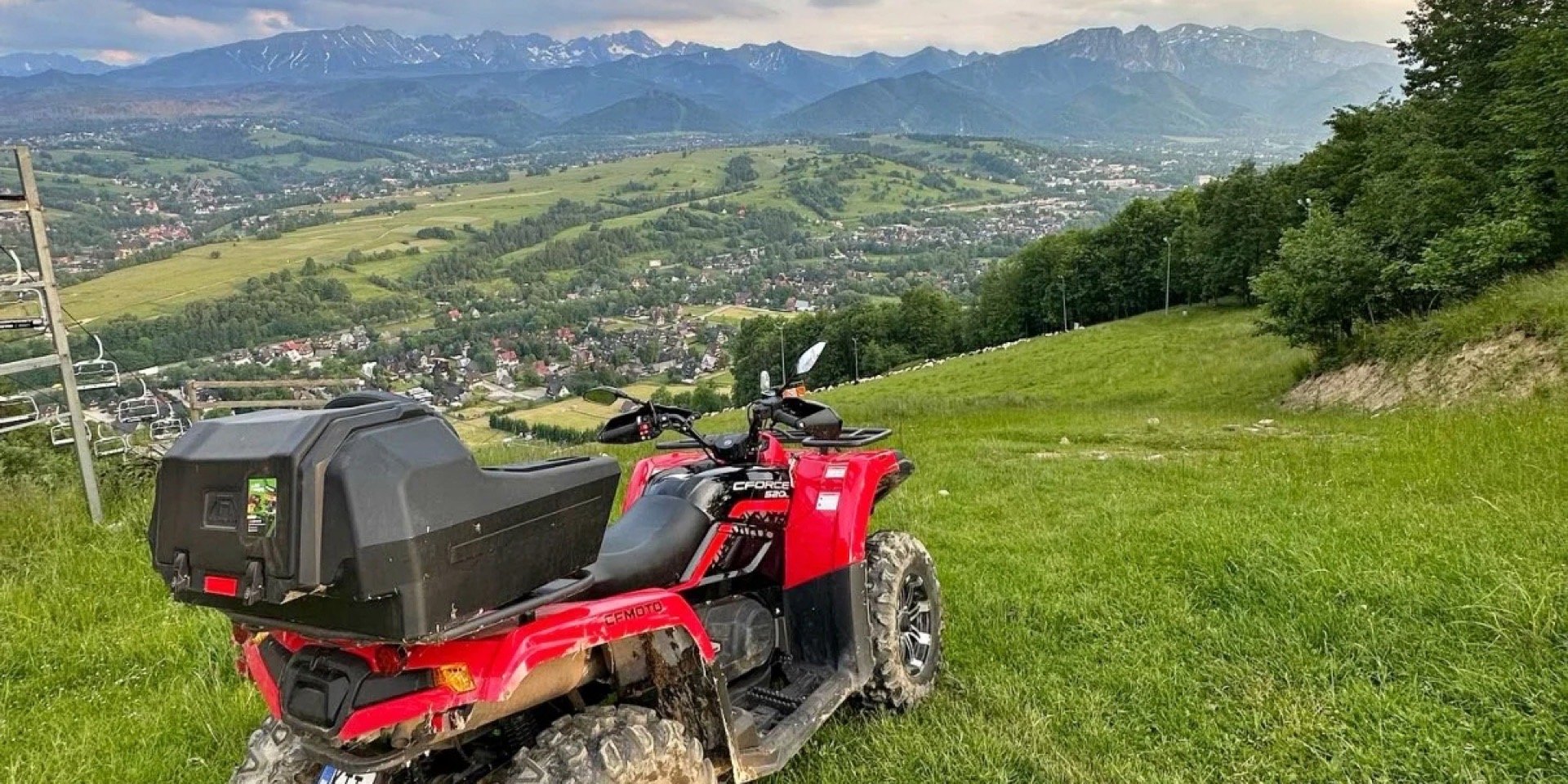 A red quad on a hillside above Zakopane, the town below and the Tatra ridge behind
